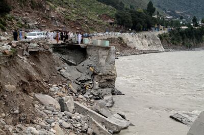 Passengers wait by a damaged road next to floodwaters in the Pakistani town of Bahrain. AP