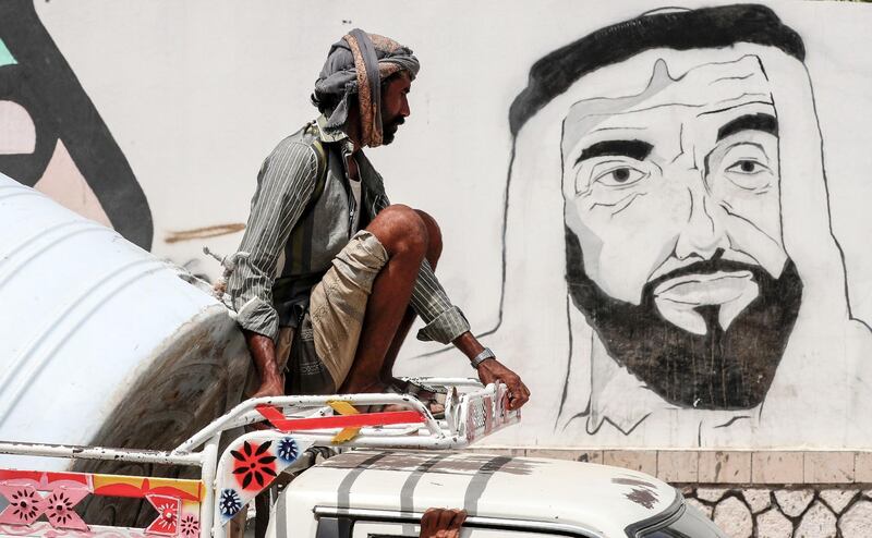 A Yemeni man riding on top of a pick-up truck driving past a mural depicting the UAE's Founding Father Sheikh Zayed in  Mukalla. AFP