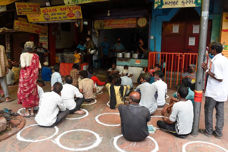 People in need sit while maintaining social distancing in front of a restaurant offering free meals in Ahmedabad. AFP