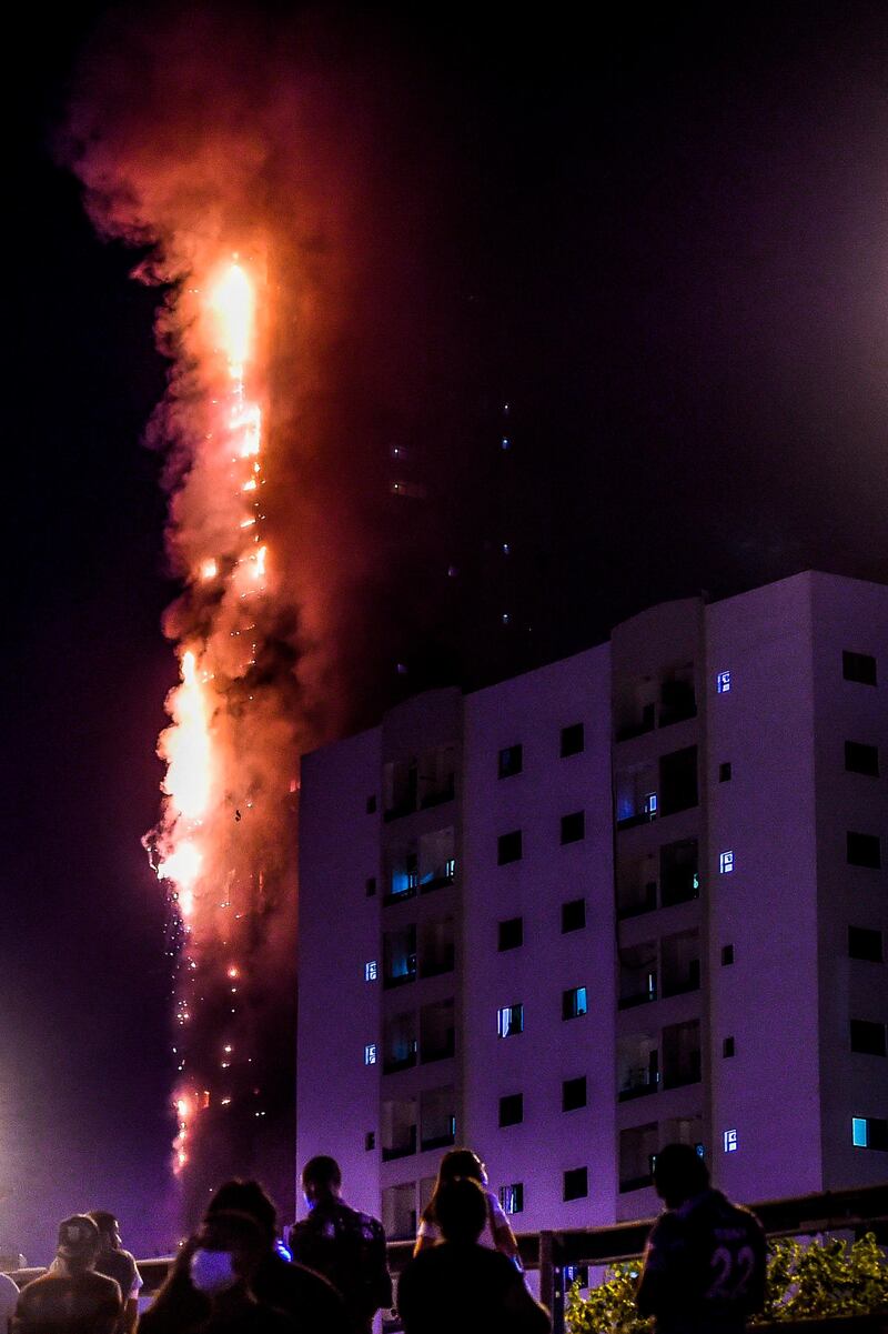 People stand on a bridge and watch a fire that erupts in a 48-storey residential tower in Sharjah. AFP