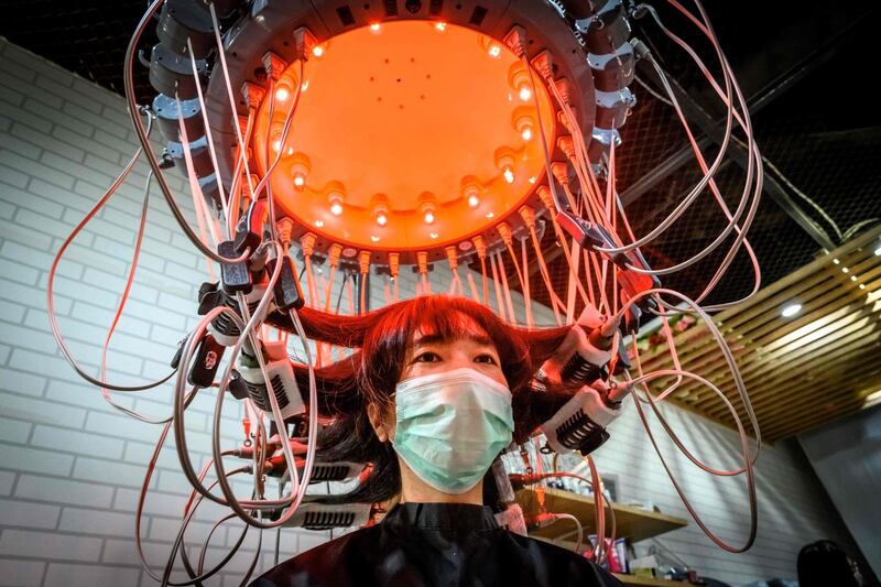 A woman wearing a face mask uses a special equipment to curl her hair at a beauty salon in Bangkok.  AFP