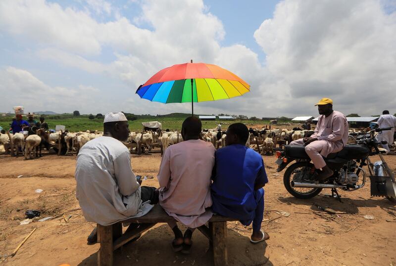 Men sit under an umbrella as they wait for customers at a livestock market in Abuja, Nigeria. Reuters