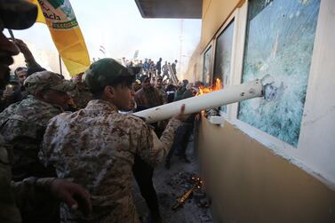Iraqi militia members use a pipe to break bulletproof glass windows at the US embassy in Baghdad on December 31, 2019. AFP