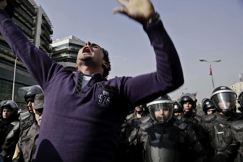 A Coptic Christian man chants slogans during a protest on Monday, December 12, 2016 as policemen stand guard on a street after a funeral service at Virgin Mary Church, Cairo for victims of the bombing during Sunday mass at a chapel adjoining  St Mark's Cathedral.  Nariman El Mofty / AP 