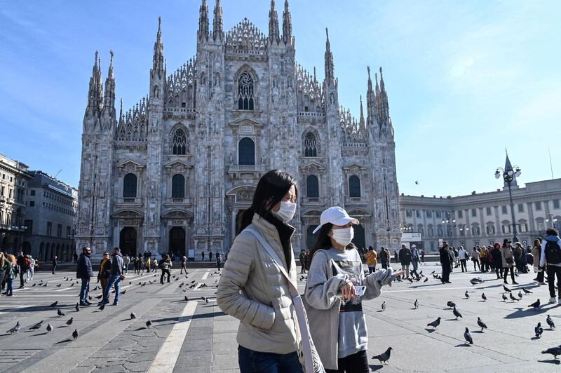 Two women wearing protective facemasks walk across the Piazza del Duomo, in front of the Duomo, in Milan, Italy. AFP