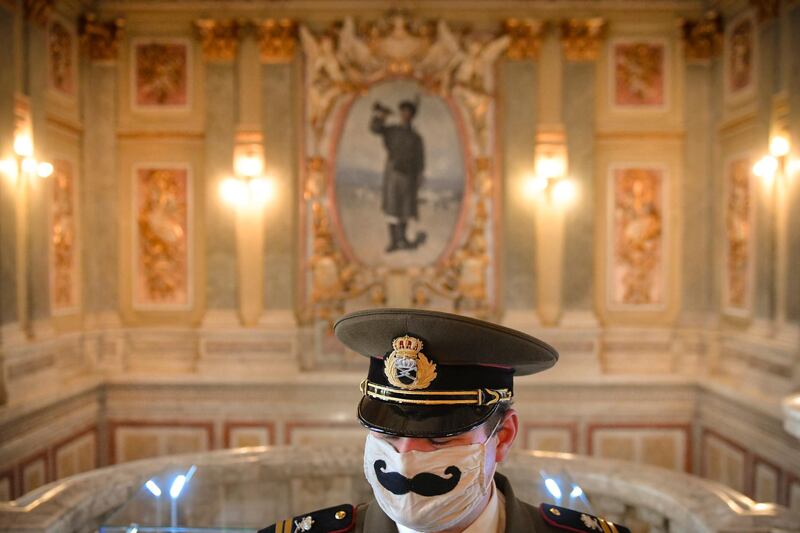 A member of an historical association wears a vintage military outfit and a COVID-19 protection mask decorated with a mustache during an event ahead of the national Veteran's Day, celebrated on April 29, at the National Military Circle, a grand 19th-century building in Bucharest, Romania, Tuesday, April 27, 2021. Servicemen, along with members of Romania's former royal family and officials including the country's Prime Minister and President took part in the packing of Easter presents that included traditional sweets and a bottle of wine for the country's war veterans and their surviving relatives. (AP Photo/Andreea Alexandru)