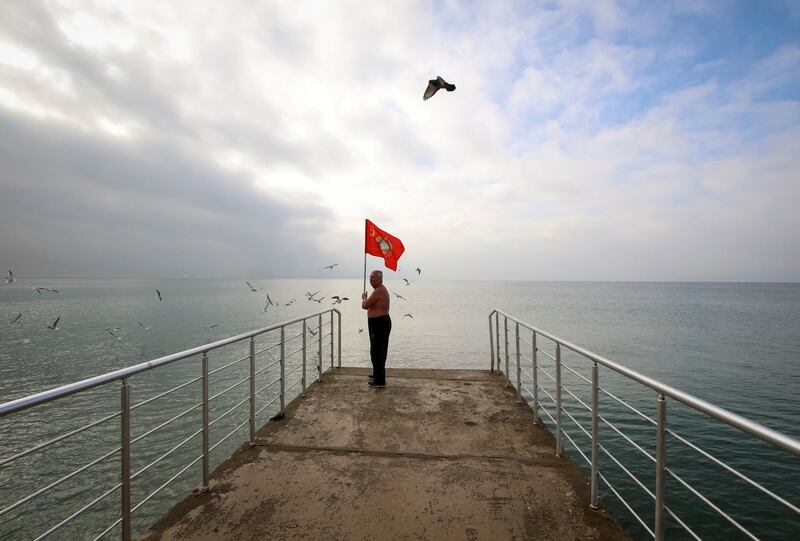 A man holds a Soviet flag as he stands on a pier during the opening of the cold water swimming season at the Black Sea town of Saky, Crimea. Reuters