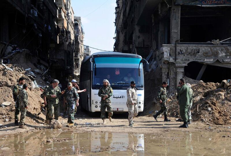 FILE - In this file photo released April 30, 2018 by the Syrian official news agency, SANA, Syrian government forces oversee a bus carrying al-Qaida-linked fighters during an evacuation from the Palestinian refugee camp of Yarmouk, near Damascus, Syria. Syria's military said Monday, May 21, 2018, that it has liberated the last neighborhoods in southern Damascus held by the Islamic State including the Palestinian Yarmouk camp and Hajar al-Aswadand and declared the Syrian capital and its surroundings "completely safe" and free of any militant presence. (SANA via AP, File)
