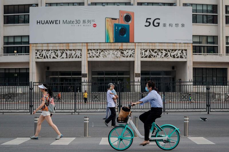 A billboard (top) featuring a commercial for Chinese telecom brand Huawei displaying their new 5G smartphones is seen as people passes by on a street in Beijing on May 22, 2020.  / AFP / NICOLAS ASFOURI
