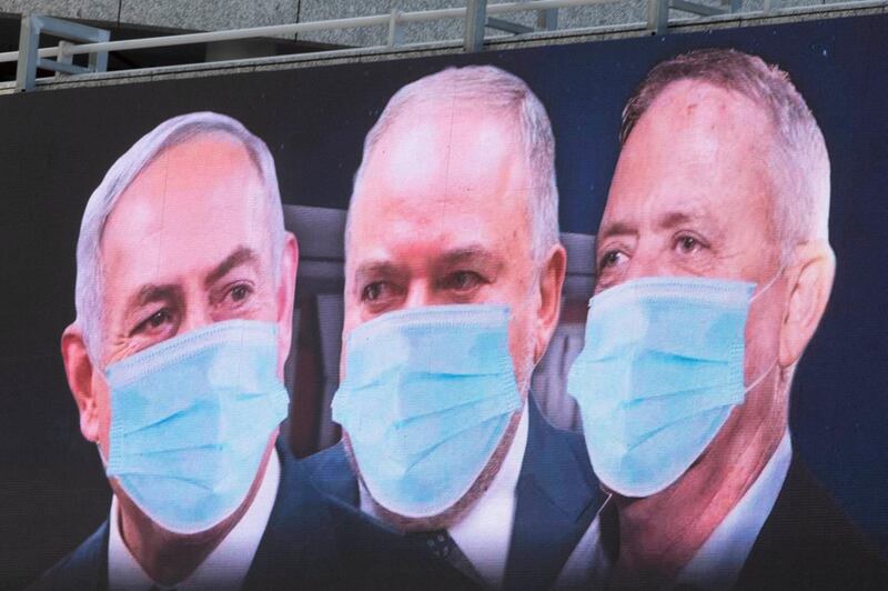 Israeli Prime Minister Benjamin Netanyahu, left, Israeli Former Defense Minister and leader of the Yisrael Beiteinu (Israel Our Home) right-wing party Avigdor Lieberman, center, and Blue and White party leader Benny Gantz, are shown on a billboard wearing masks in the Israeli city of Ramat Gan, near Tel Aviv, Sunday, March 29, 2020. Gantz, Netanyahu's chief rival, was chosen on Thursday as the new speaker of parliament, an unexpected step that could pave the way to a power-sharing deal between the two men as the country grapples with a worsening coronavirus crisis. The billboard calling for unity reads: "Benny, Avigdor and Bibi take off your masks, the people want unity." (AP Photo/Sebastian Scheiner)