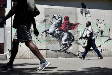 epa06841358 People walk by a recent artwork believed to be attributed to Banksy showing Napoleon rearing his horse, wrapped in a red cloak in the 19th district of Paris, France, 26 June 2018. Several artworks attributed to the anonymous British street artist appeared in the French capital over the last few days. EPA-EFE/JULIEN DE ROSA