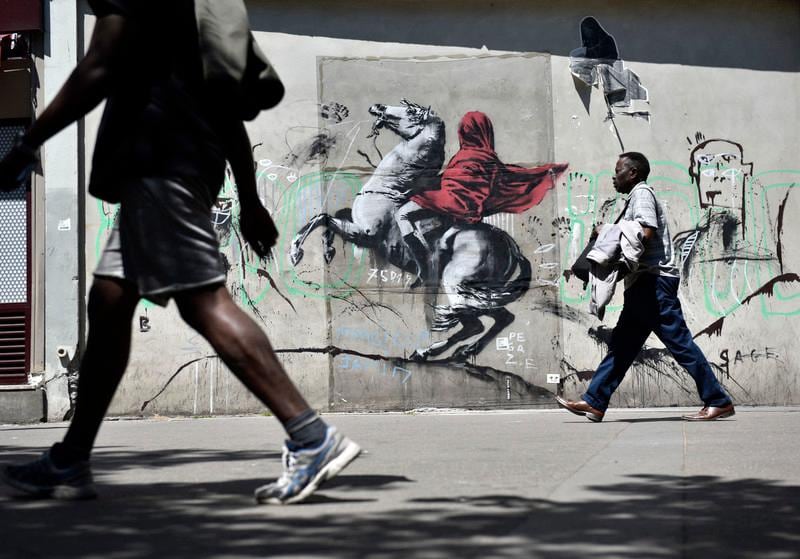 epa06841358 People walk by a recent artwork believed to be attributed to Banksy showing Napoleon rearing his horse, wrapped in a red cloak in the 19th district of Paris, France, 26 June 2018. Several artworks attributed to the anonymous British street artist appeared in the French capital over the last few days.  EPA-EFE/JULIEN DE ROSA