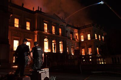 Policemen watch as a massive fire engulfs the National Museum in Rio de Janeiro, one of Brazil's oldest, on September 2, 2018. - The cause of the fire was not yet known, according to local media. (Photo by Carl DE SOUZA / AFP)