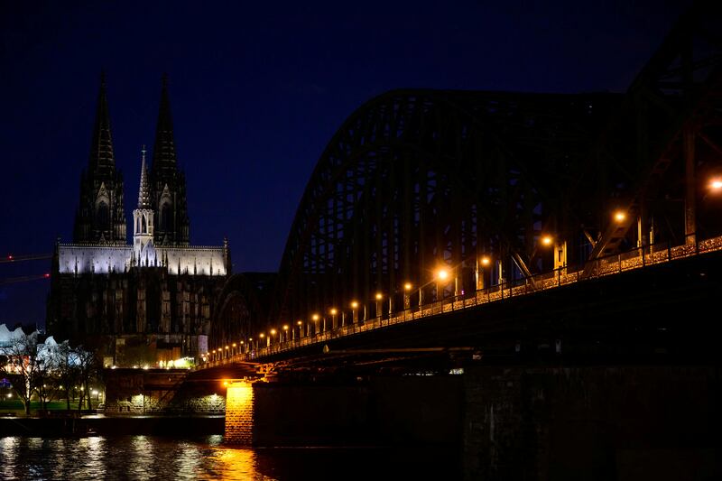 The Cologne Cathedral, a UNESCO World Heritage Site, next to the Hohenzollern railway bridge across the river Rhine, is partly illuminated during Earth Hour in Cologne, Germany, March 23, 2024.  REUTERS / Jana Rodenbusch