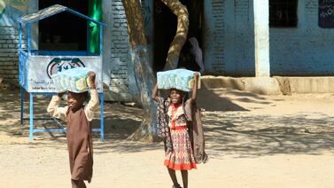 Children carry packs of humanitarian aid at a school housing people displaced by war, near the eastern city of Gedaref, Sudan. AFP