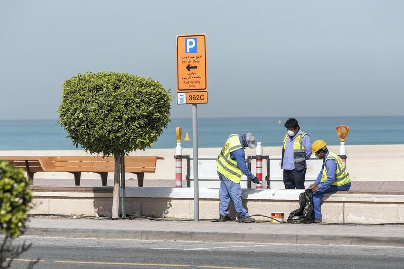 DUBAI, UNITED ARAB EMIRATES. 01 APRIL 2020. An empty Sunset Beach located between the Jumeirah Beach Hotel and Kite Beach with the ongoing Stay At Home policy being enforced on a National level in the UAE. Municipal workers paint a cement wall bench along the walking path while wearing masks. (Photo: Antonie Robertson/The National) Journalist: Standalone. Section: National.
. 
