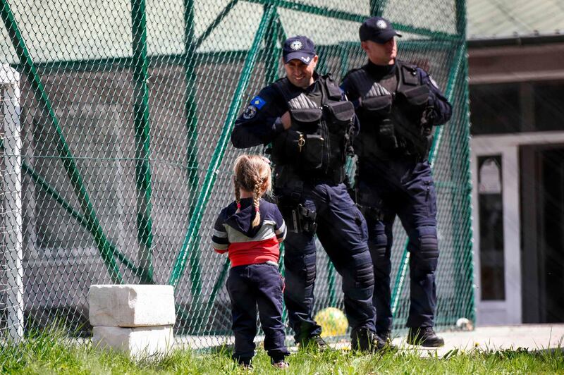 A young Kosovar child looks at Kosovar police officers as she picks up flowers in the compound of the foreign detention center in the village of Vranidoll, Kosovo, on April 20, 2019.  Kosovo on April 20, 2019 repatriated 110 of its citizens from Syria, mostly mothers with their children having followed their partners who went to join jihadist groups in the war-torn country. / AFP / Armend NIMANI
