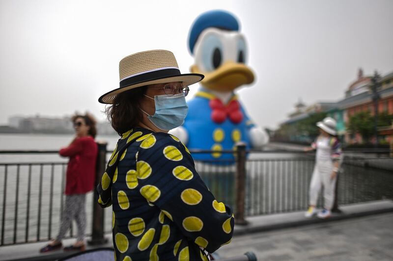 A mask-less Donald Duck stands with tourists, some with face masks and others without.  AFP