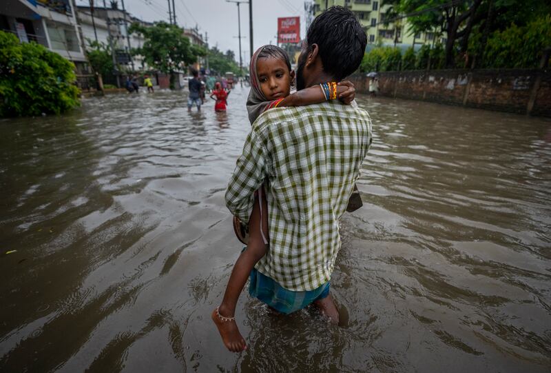 A man carries his child as he wades through floodwaters on a road in Guwahati. AP  