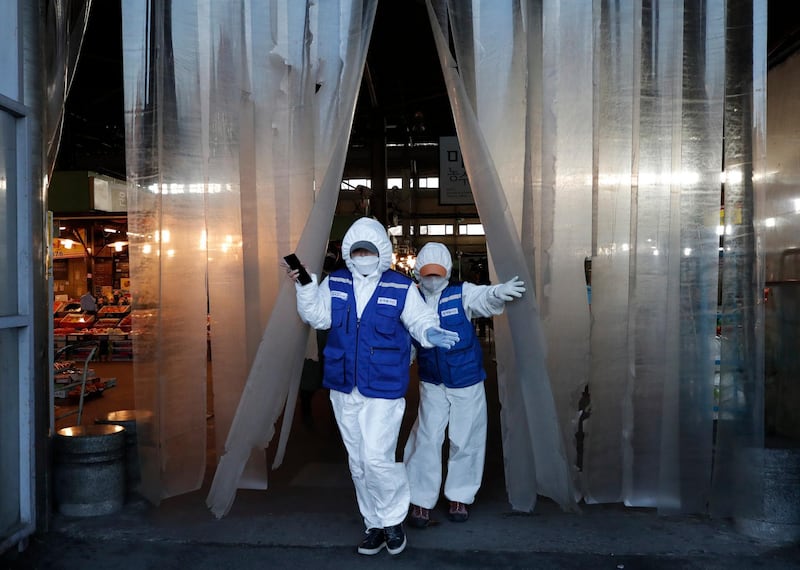 Workers wearing protective suits walk before they spray disinfectant as a precaution against the COVID-19 at a market in Seoul, South Korea, AP