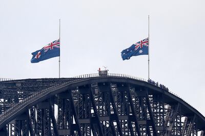 People climbing the Sydney Harbour Bridge stop under flags flying at half-mast as mark of mourning and respect in Sydney, Australia, Friday, Jan. 24, 2020, for three U.S. crew members of an aerial water tanker that crashed Thursday while battling wildfires in Australia. (AP Photo/Rick Rycroft)