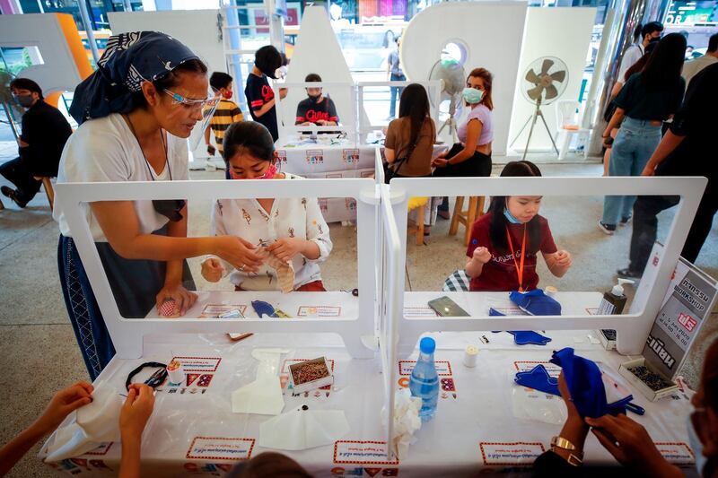 People are separated by plastic partitions to ensure minimum social distancing as they make protective face masks for children with cloth at a fair in Bangkok, Thailand.  EPA