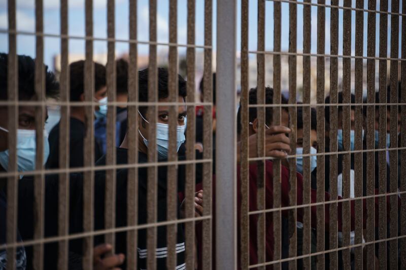 Migrants who were intercepted crossing the Mediterranean by boat line up behind a fence in Lampedusa, Italy, as they wait to board a ferry to Sicily.