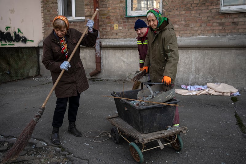Residents clean the street outside apartments damaged by shelling, in Kyiv, Ukraine. AP
