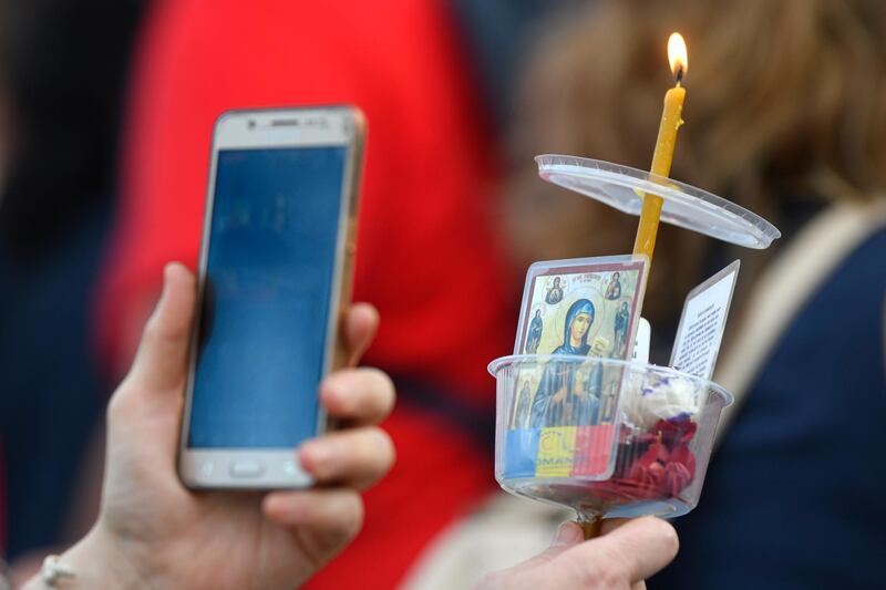 A woman holds a lit candle, icons and a mobile phone during a protest against the use of face masks and the protection measures against the COVID-19 infections in Bucharest, Romania, Saturday, Oct. 10, 2020. Several hundred Romanians, mostly Orthodox Christian zealots and right-wing nationalists, held a protest in the country's capital against measures meant to curb the spread of the coronavirus, especially social distancing and the mandatory use of masks in schools, as Romania registered the highest numbers of COVID-19 daily infections and deaths since the start of the pandemic. (AP Photo/Andreea Alexandru)