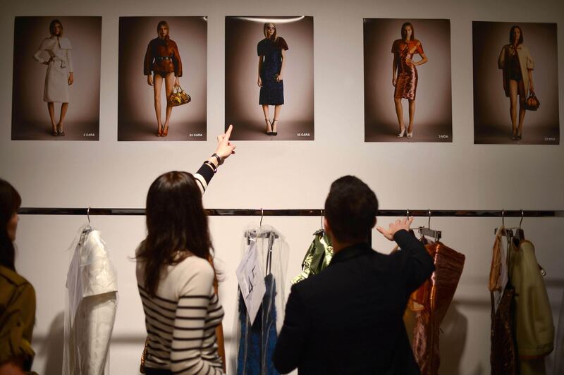 A model points at a poster as dresses are prepared backstage ahead of the Burberry Prorsum 2013 spring/summer collection catwalk show during London Fashion Week in London on September 17, 2012. AFP PHOTO / BEN STANSALL