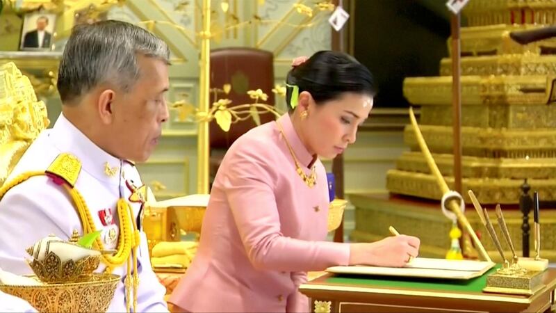 King Maha Vajiralongkorn watches Queen Suthida sign their marriage certificate.