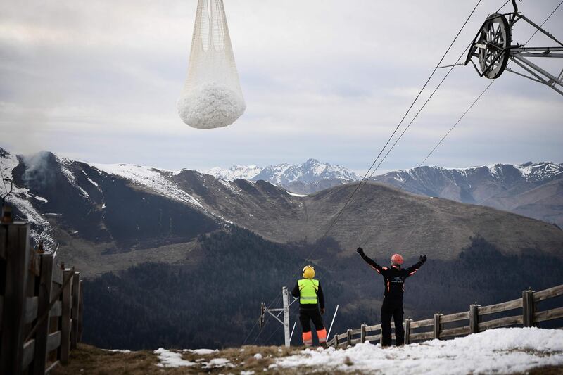 Two men help an helicopter carrying snow in order to place it on a ski slope in the Superbagneres station, near Luchon, in French Pyrenees mountain southwestern France, on February 15, 2020. The French department of Haute-Garonne decided to pour snow by helicopter on the Luchon-Superbagneres station in order to make up for the lack of snow on February 14 and February 15, 2020. / AFP / Anne-Christine POUJOULAT
