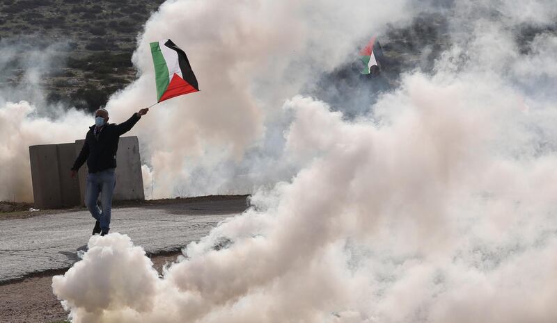 A Palestinian protester waves a Palestine flag as he seeks cover from tear gas during clashes at Tayaseer checkpoint. According to reports, 55 Palestinians were wounded during clashes that erupted as they attempted to cross the checkpoint during a protest against the Israeli settlements. EPA