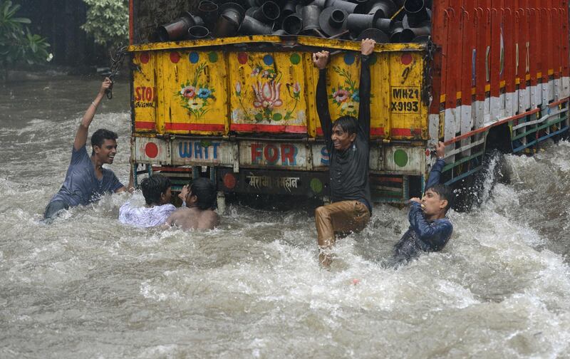 Indian men cling on to  the back of a lorry driving through floodwaters after heavy rain in Mumbai. Punit Paranjpe / AFP Photo