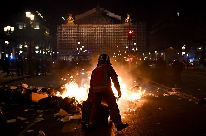 A firefighter holds a bin as he stands next to a burning pile of rubbish in front of Opera Garnier during a demonstration a few days after the government pushed a pensions reform through parliament without a vote, using the article 49,3 of the constitution in Paris on March 20, 2023.  - The French government survived two no-confidence motions in parliament on March 20, 2023 but still faces intense pressure over its handling of a controversial pensions reform.  (Photo by Christophe ARCHAMBAULT  /  AFP)