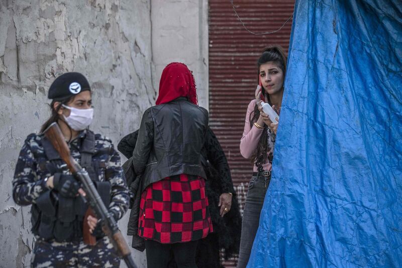 A member of Kurdish Internal Security stands guard as Kurdish Red Crescent medics check a passenger for Covid-19 symptoms upon arrival from the Syrian capital, at a mobile site just outside Syria's Qamishli airport in the northeastern Hasakeh province.  AFP