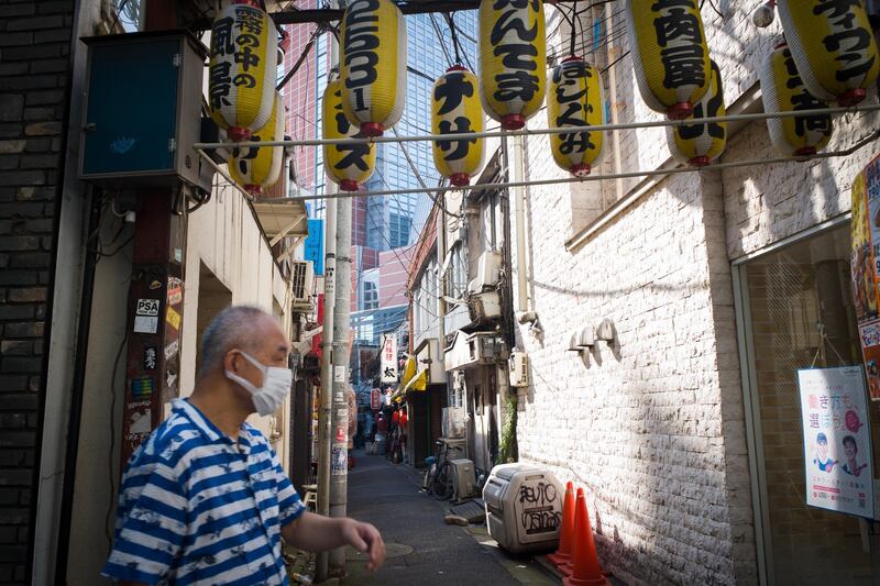 A pedestrian wearing a protective face mask walks past an empty alley in the Setagaya district of Tokyo, Japan, on Sunday, August 2, 2020. Japan’s economy shrank at the same pace as previously estimated, according to revised data that continued to show the country was in a recession before the pandemic took its heaviest toll. Photographer: Kentaro Takahashi/Bloomberg