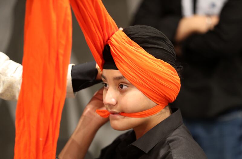 A young member of the Sikh community gets his turban prepared for the party.