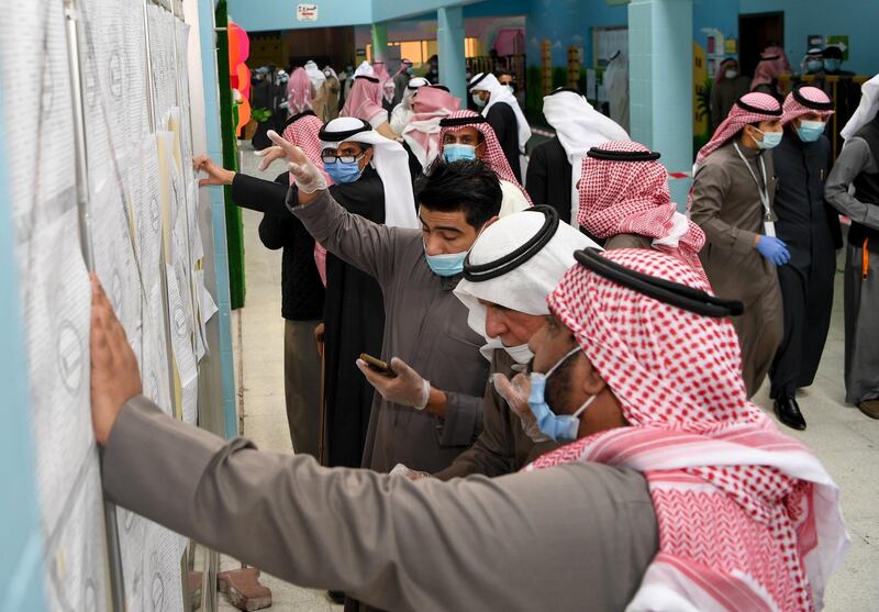 People wearing protective masks searches for her name on a voter list at a polling station in Kuwait City. EPA