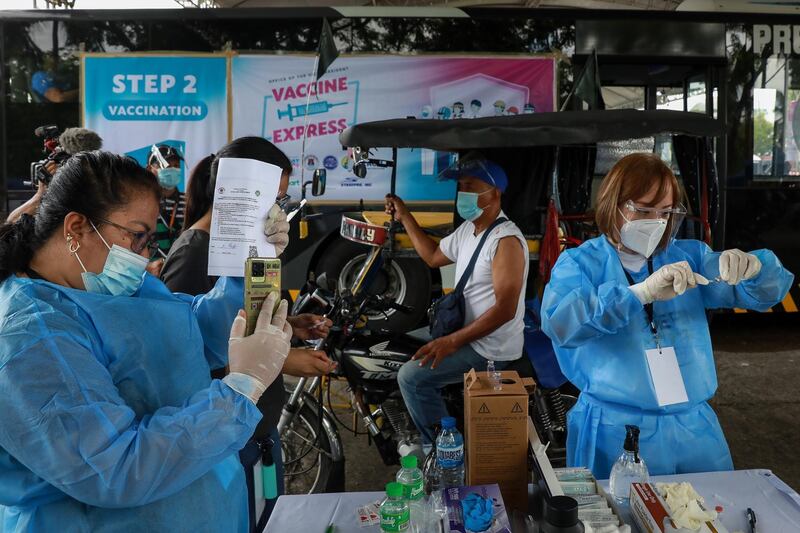 A health worker scans the QR code of a tricycle driver, centre, as another health worker prepares a Sinovac Covid-19 vaccine dose at a parking lot in Manila, Philippines. EPA