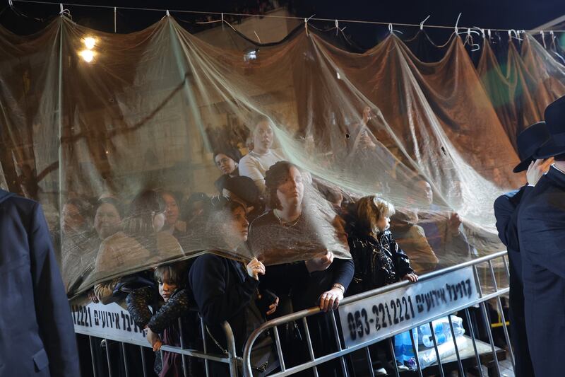 Ultra-Orthodox women watch from behind a curtain as men gather round a bonfire in the neighborhood of Mea Shearim during the holy day of Lag Ba'Omer in Jerusalem. EPA
