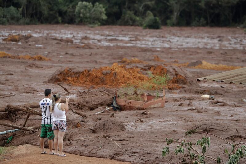 A couple with missing relatives look at the flooded area, after a dam collapsed in Brumadinho, Brazil, Saturday, Jan. 26, 2019. An estimated 300 people were still missing and authorities expected the death toll to rise during a search made more challenging by intermittent rains. (AP Photo/Andre Penner)