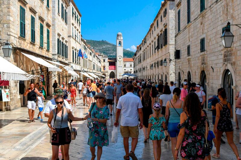 Tourists stroll in a street as they visit the centre of Dubrovnik on August 6, 2018. - Montenegro's medieval walled city of Kotor, an Adriatic seaport cradled in a spectacular fjord-like bay, has survived centuries of weather and warfare. Now it is facing a different kind of assault, that of gargantuan cruise ships disgorging throngs of tourists threatening a place that was only a few years ago commonly described as a "hidden gem". (Photo by Savo PRELEVIC / AFP)