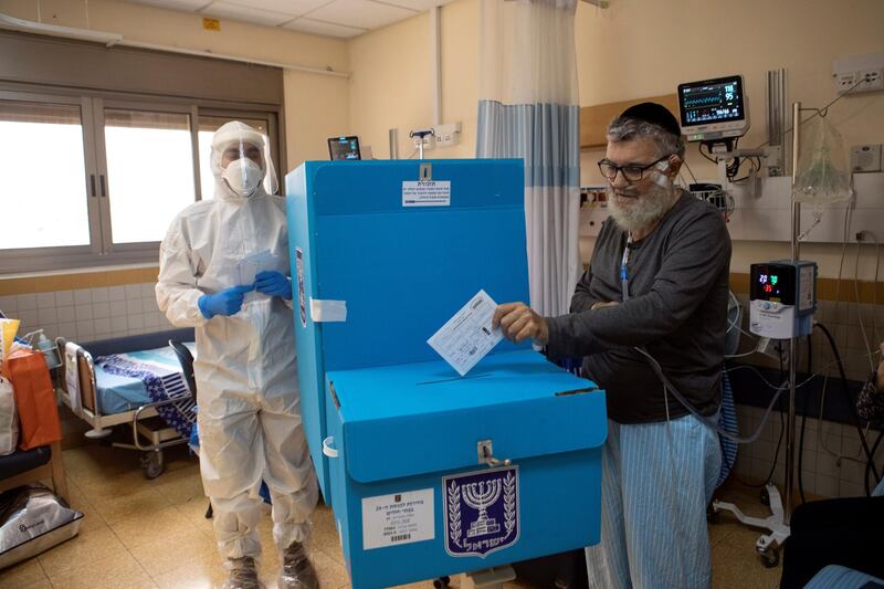 A hospital employee wearing PPE, watches while a patient in a ward for the treatment of the coronavirus disease, casts his ballot in a mobile ballot box as Israelis vote in a general election, at Sheba Medical Center in Ramat Gan. Reuters