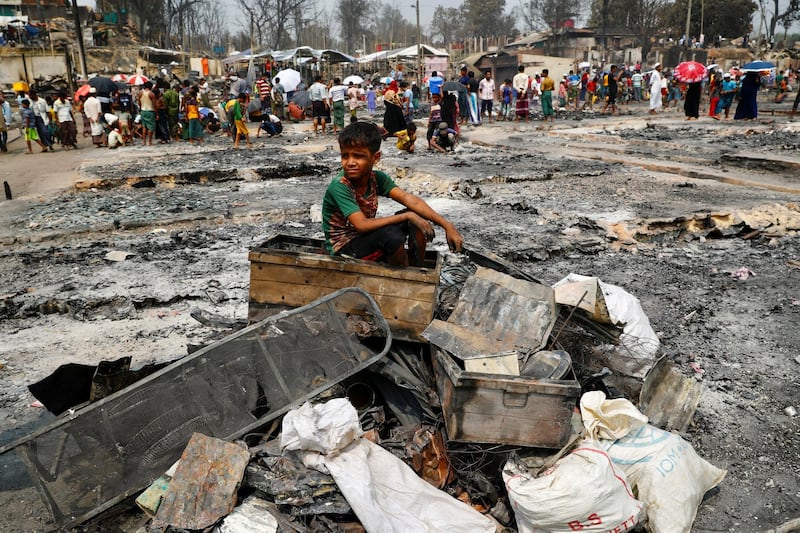 A Rohingya refugee boy on a stack of burnt material after a fire broke out and destroyed thousands of shelters in a Rohingya refugee camp in Cox's Bazar, Bangladesh on March 24, 2021. Reuters