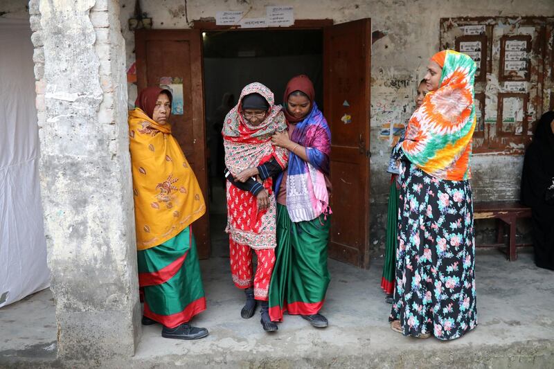 A government official helps an elderly women step out from a voting center in Dhaka. Reuters