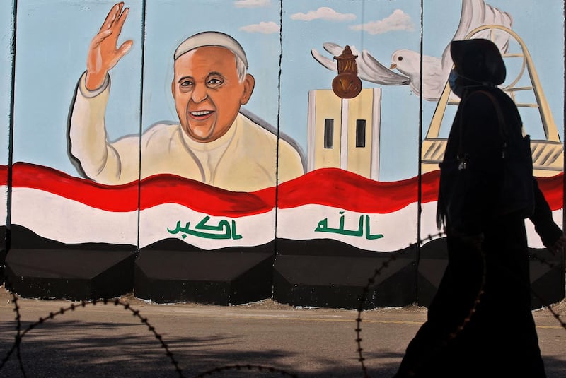 An Iraqi woman walks by a mural depicting Pope Francis on the security wall around Our Lady of Salvation Church in Baghdad. EPA