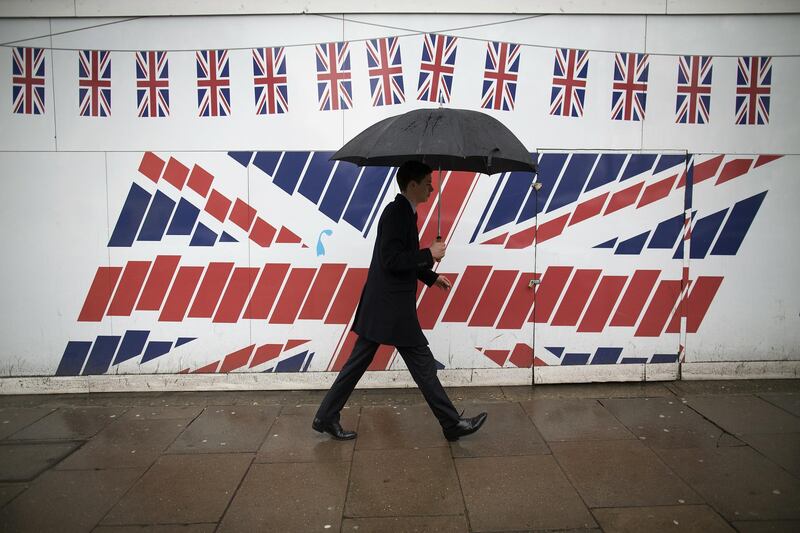 FILE: A pedestrian shelters from the rain beneath an umbrella as he passes construction hoardings decorated with British Union Jack flags in London, U.K., on Thursday, March 7, 2013. European Union and Jack flags as Brexit trade talks that were on the verge of a breakthrough descended into a fight between the U.K. and France on Thursday as the British government said prospects of an imminent deal had receded. Photographer: Simon Dawson/Bloomberg