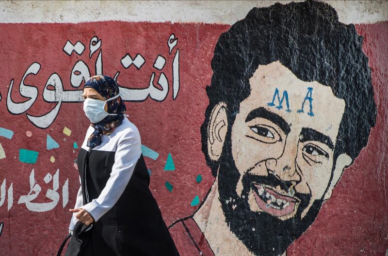 A woman wearing a protective mask walks in front of a mural depicting Liverpool's Egyptian striker Mohamed Salah in Cairo in March. The Egyptian Football Association announced Salah has tested positive for coronavirus. EPA