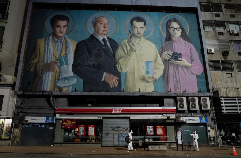 City workers disinfect a bus stop to help prevent the spread of coronavirus outside a closed cinema featuring a mural of film directors, from left, Federico Fellini, Alfred Hitchcock, Luis Buñuel and Lucrecia Martel in Montevideo, Uruguay. AP Photo